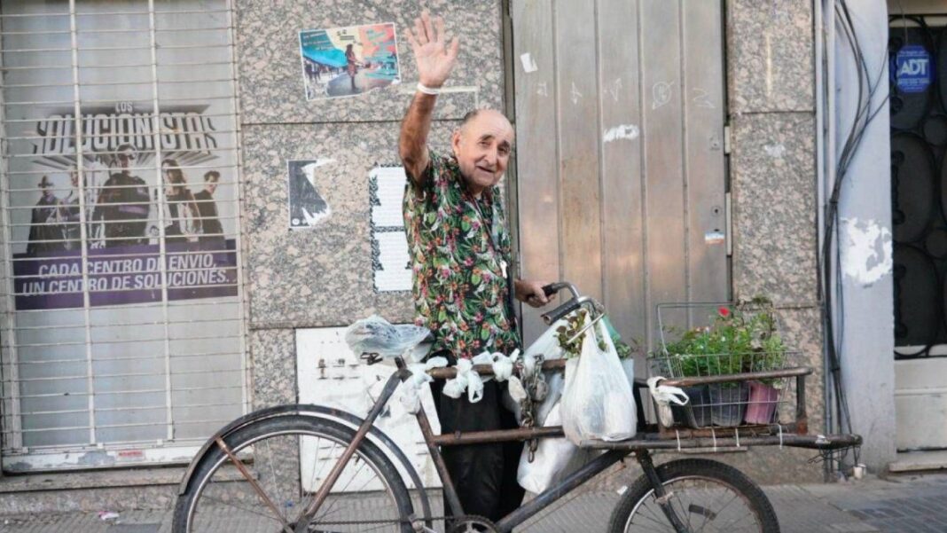 Nino, un hombre mayor, sonriendo junto a su bicicleta cargada de plantines en una calle de Rosario.