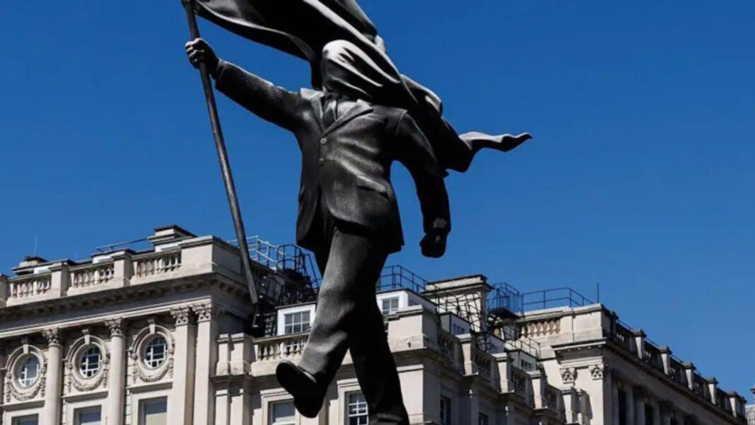 Estatua de Banksy en Waterloo Place, Londres, con un hombre de traje y una bandera cubriendo su rostro