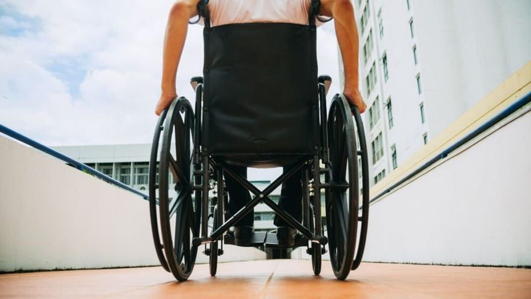 Persona en silla de ruedas junto a un profesional de la salud en un centro de rehabilitación